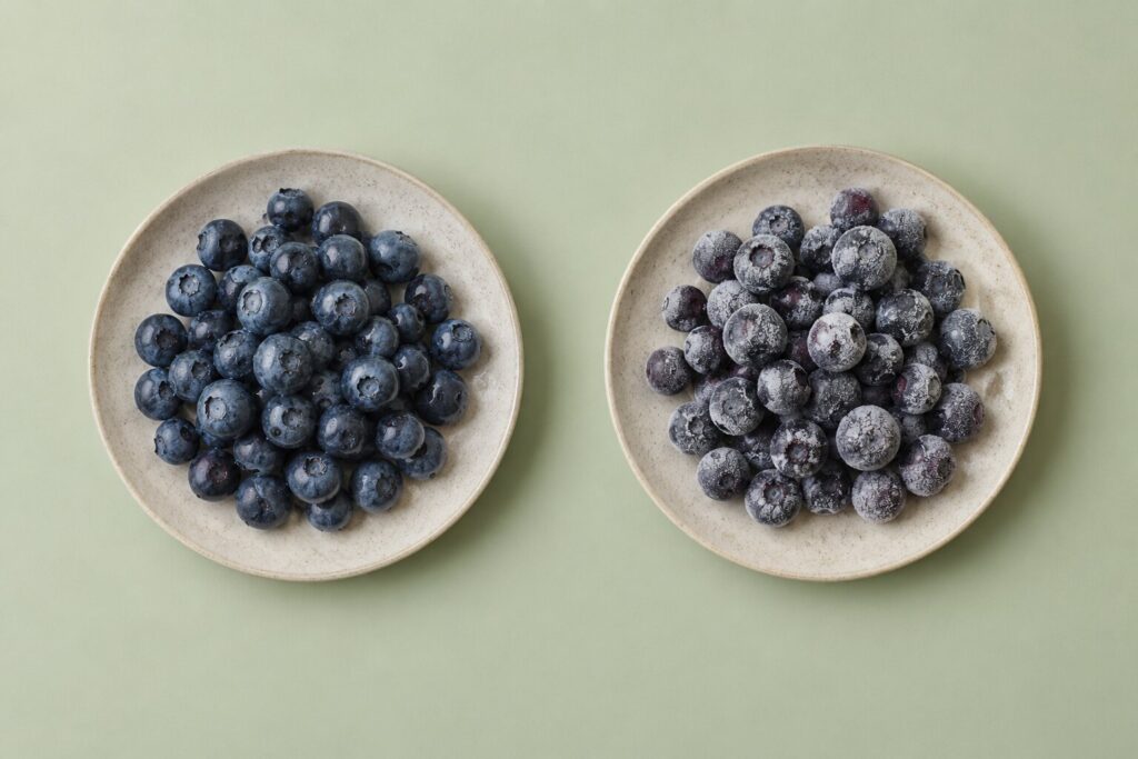 Can Dogs Eat Blueberries? 2 Fresh blueberries and frosty frozen blueberries sit separately on plain stoneware plates.