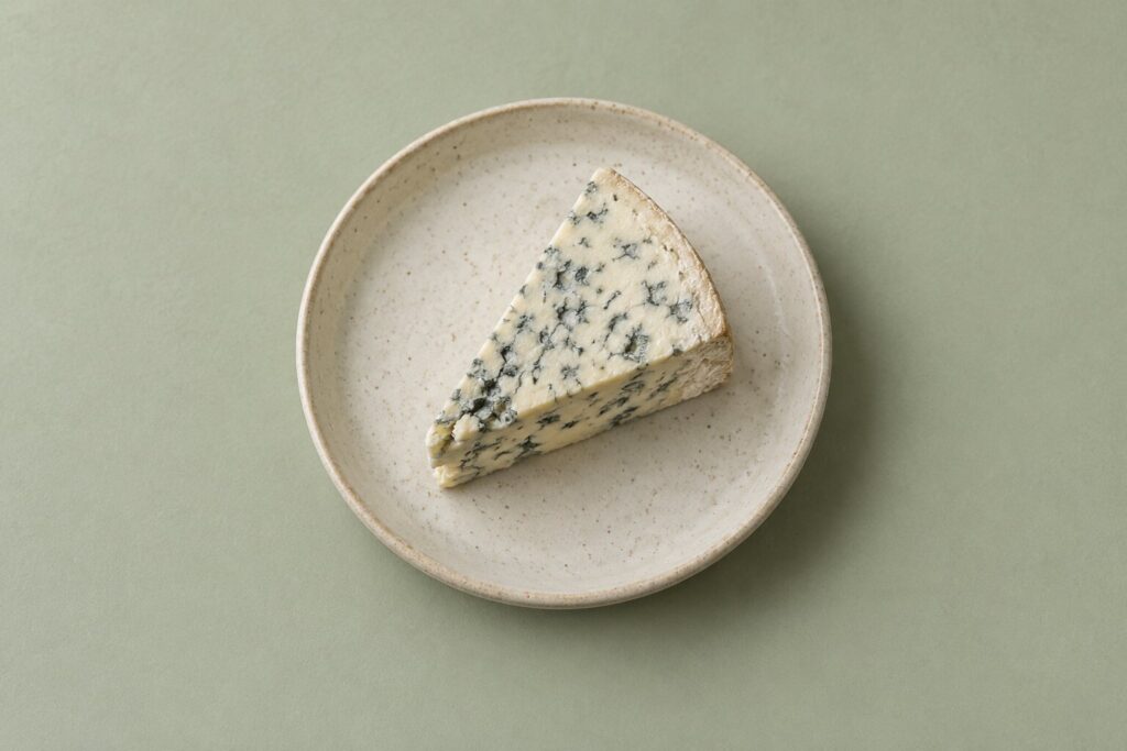 Can Dogs Eat Cheese? 1 A small wedge of blue cheese rests alone on a plain ceramic dish.