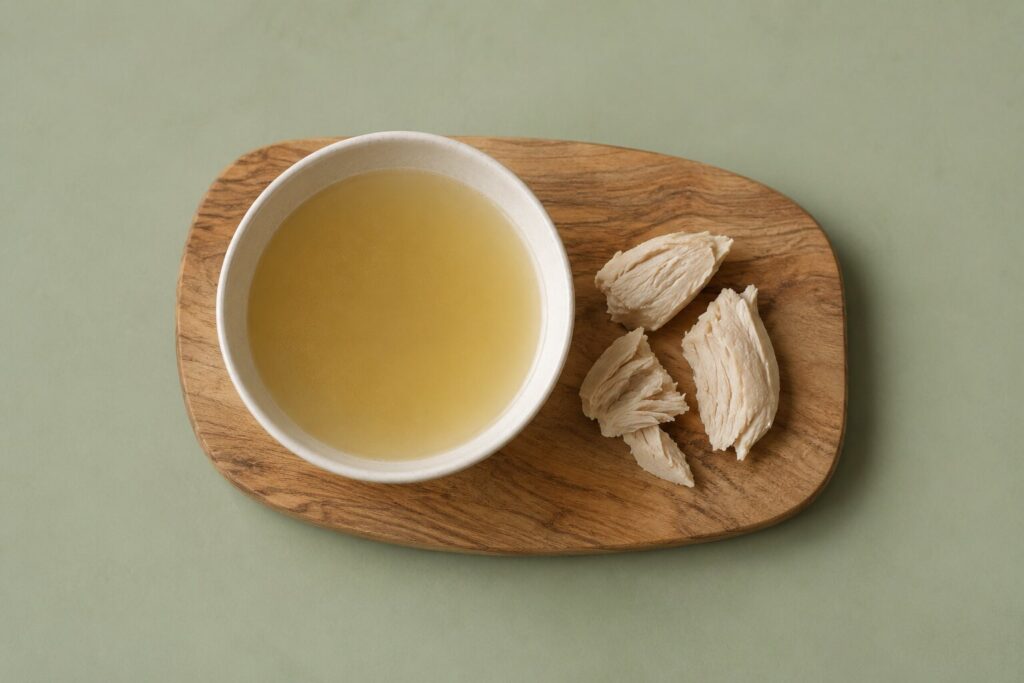 Can Dogs Eat Chicken? 2 A bowl of clear chicken broth sits beside cooked chicken on a wooden board.