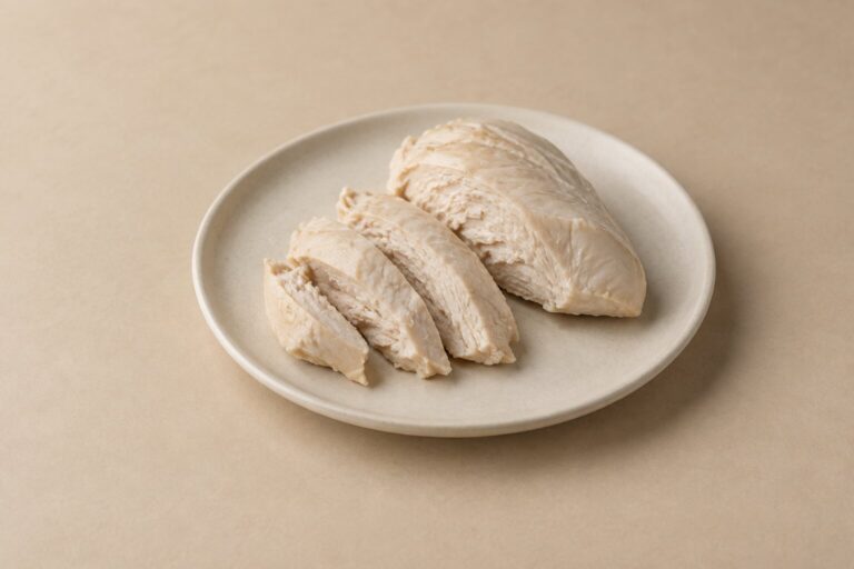 Plain cooked chicken breast pieces arranged on an ivory plate against a warm oat backdrop.