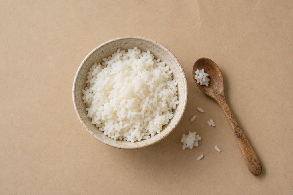 A ceramic bowl of plain cooked white rice on a warm oat background