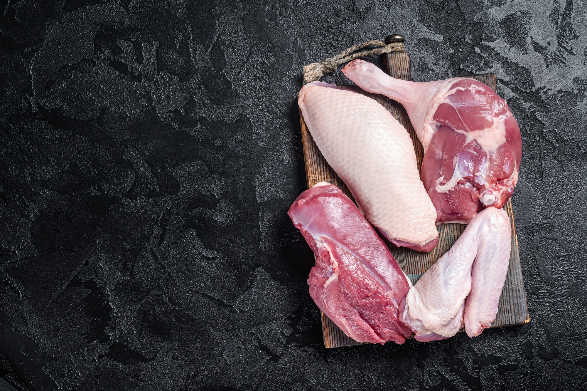 Duck breast fillet, legs, wings, raw meat on a butcher cutting board. Black background