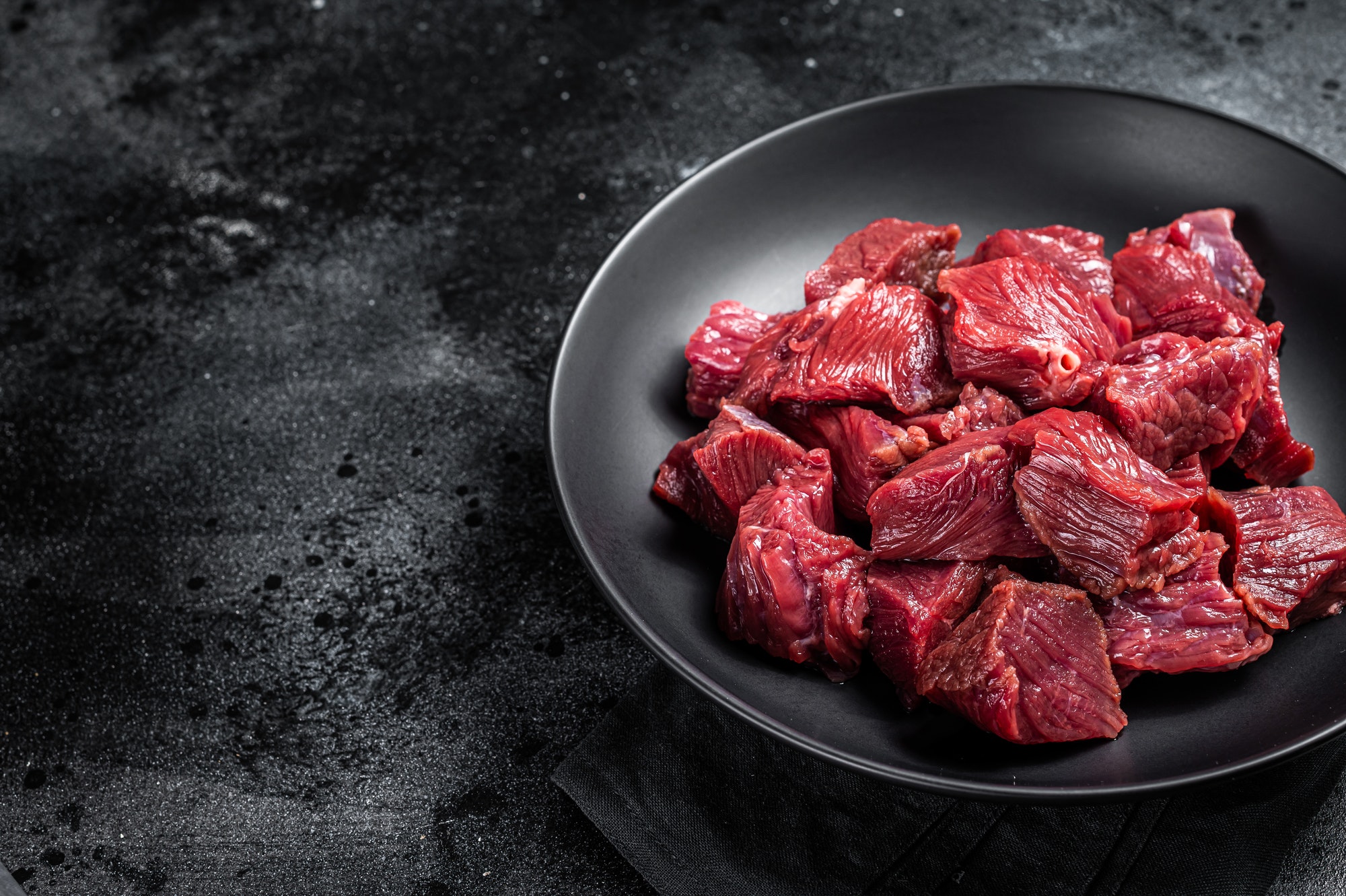 Raw Diced game meat of wild venison dear. Black background. Top view. Copy space
